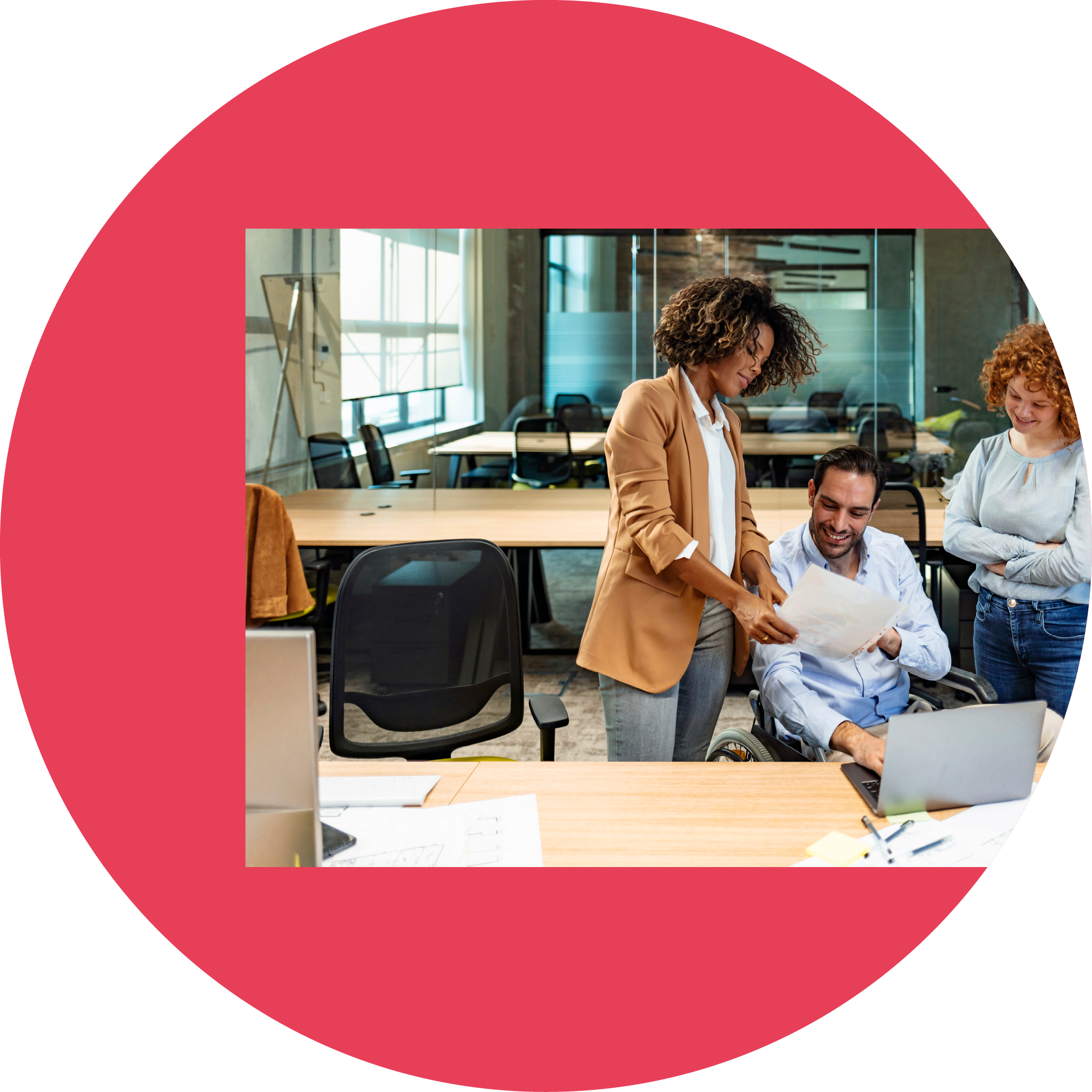 One Businessman on a wheelchair sitting at the table with his two female colleagues standing next to him in the office 