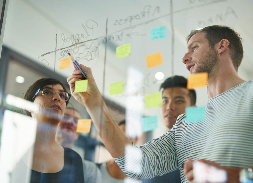 Cropped shot of coworkers using sticky notes on a glass wall during a meeting